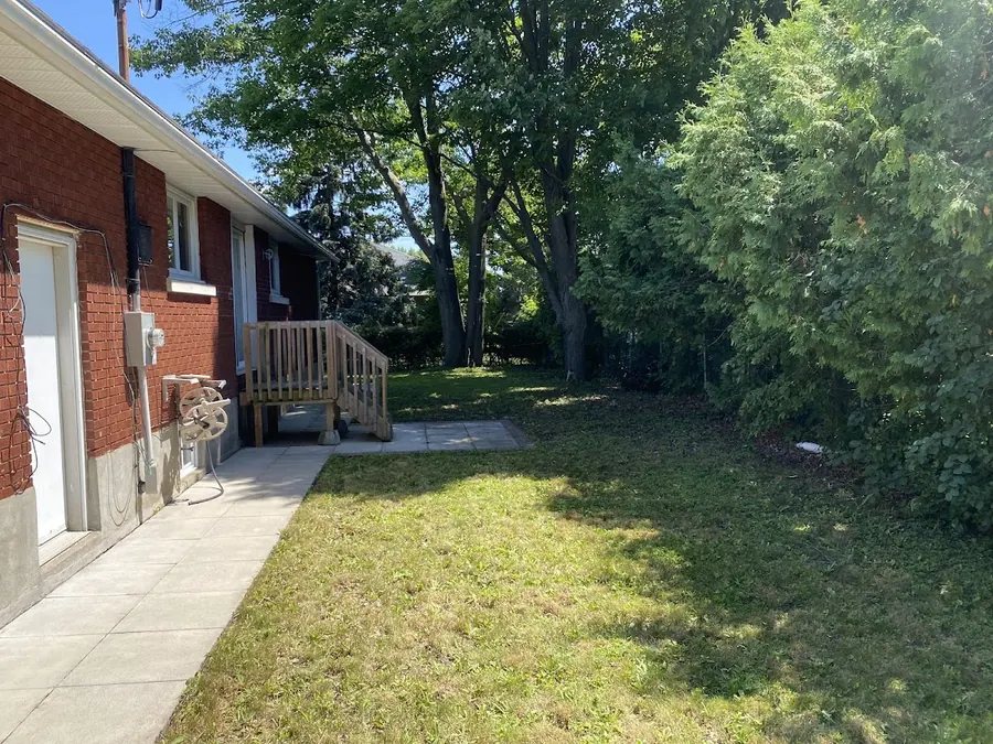 A trimmed backyard lawn beside a brick house with tall trees behind
