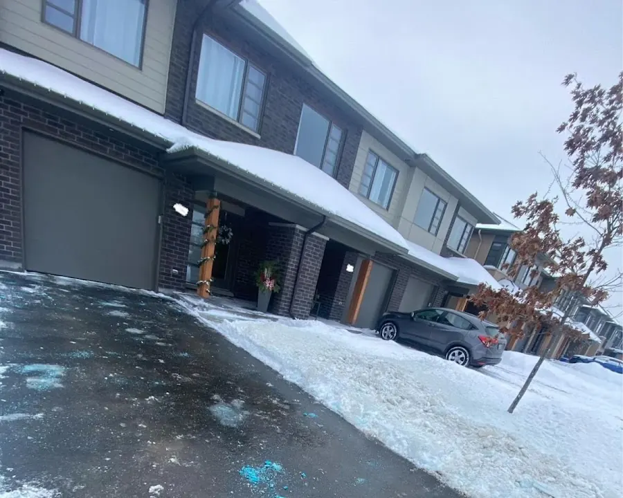 A plowed black driveway between banks of snow in front of a row of townhouses
